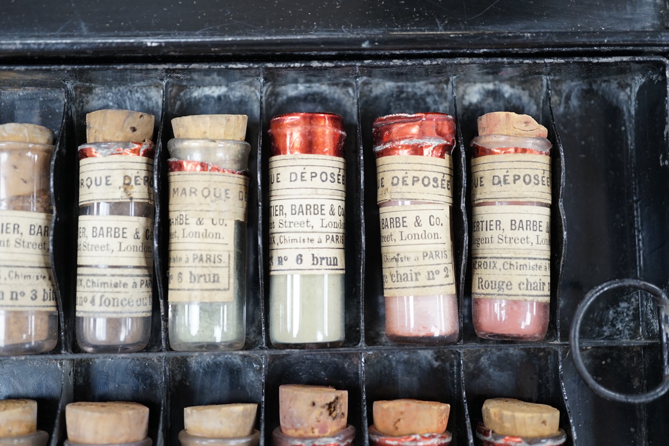 A black artist's tin box, with fitted interior, containing glass phialls of coloured shades of powdered paint and a white glass samples panel etc, box 37.5cm wide, 27cm deep